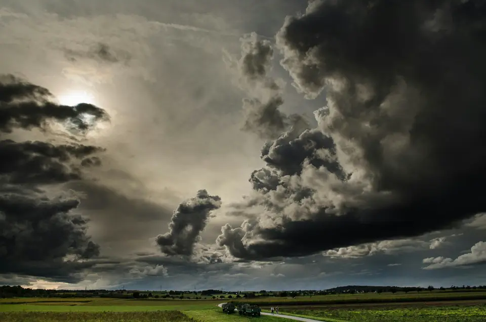 Dark, dramatic storm clouds over a flat, green countryside with a narrow road.